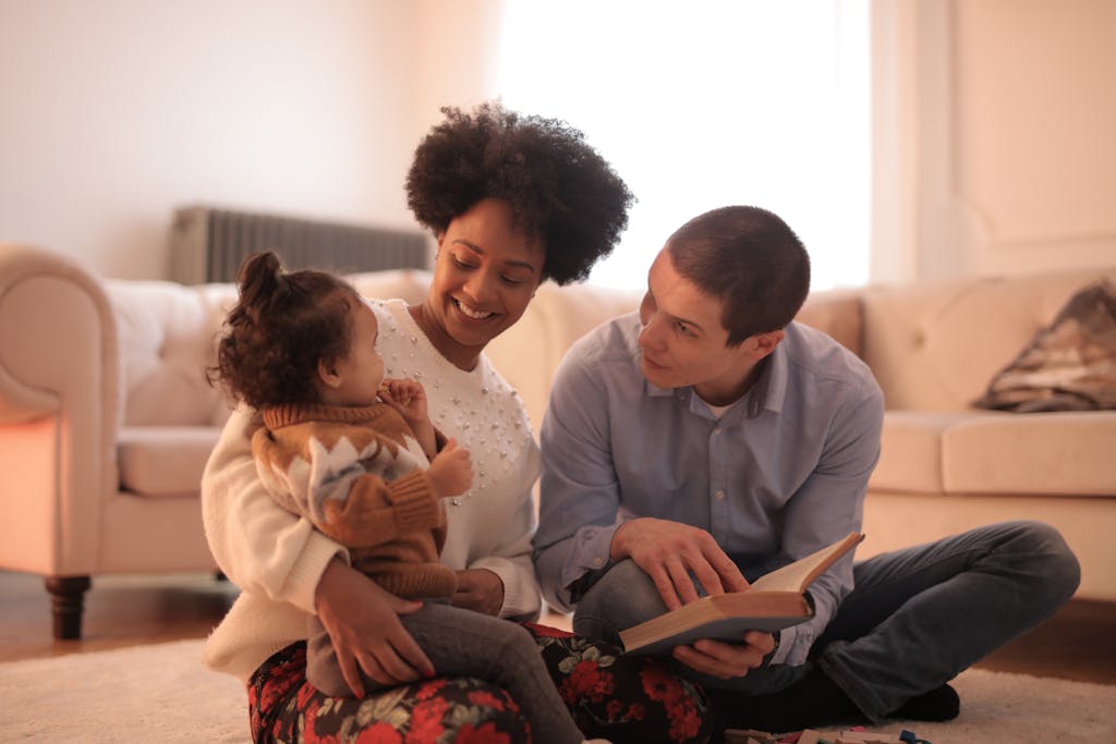 Loving parents reading with cheerful toddler in cozy living room, embracing family time.